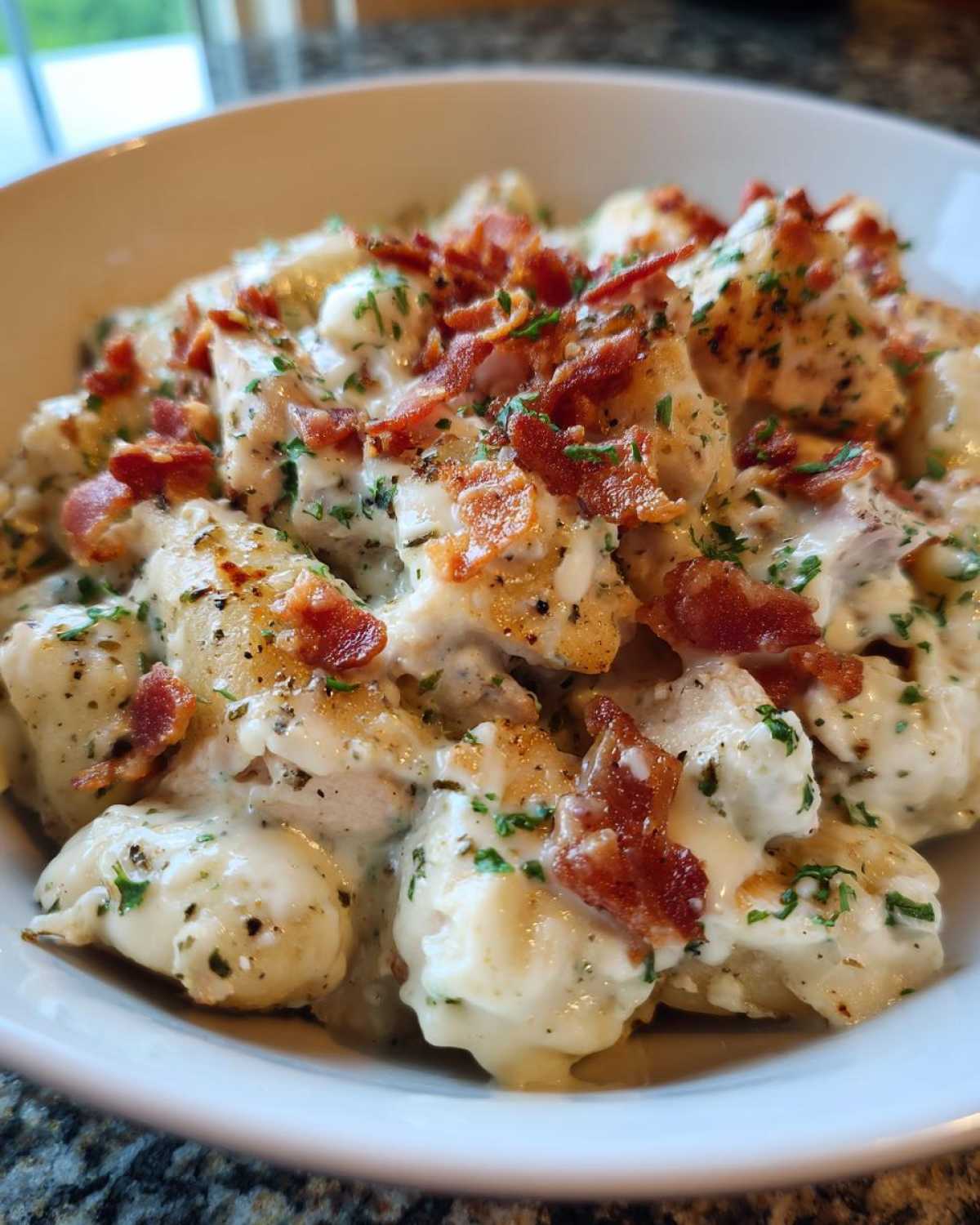A close-up of creamy crack chicken gnocchi coated in a rich white sauce, topped with crispy bacon bits and fresh parsley.