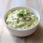 A close-up of creamy dill pickle dip, chunky with pickles and topped with fresh dill.