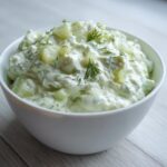 A white bowl filled with creamy dill pickle dip, garnished with fresh dill sprigs.