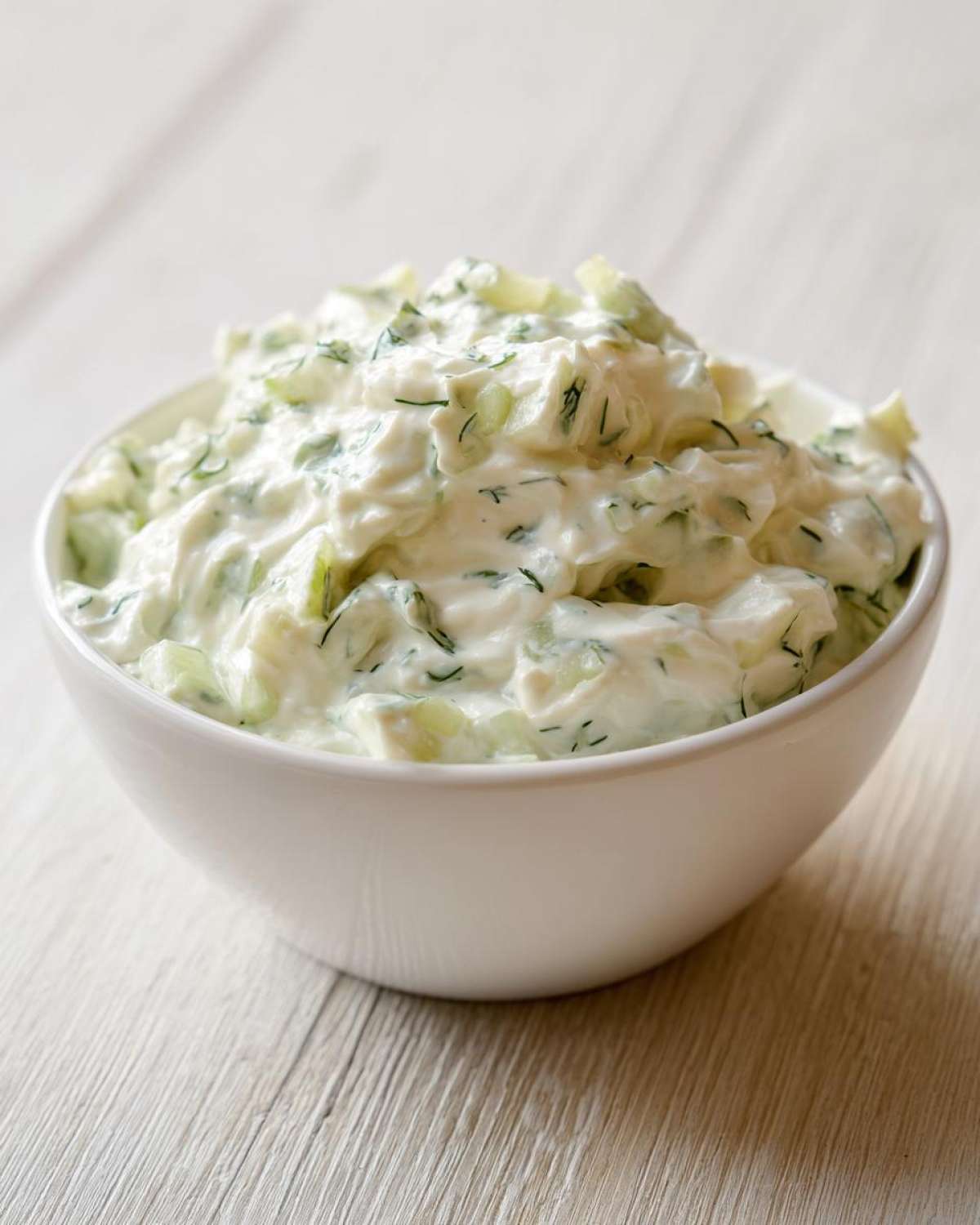 Close-up of creamy dill pickle dip loaded with chopped pickles and fresh dill in a white bowl.