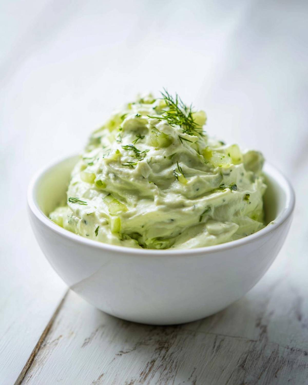 A close-up of creamy dill pickle dip topped with fresh dill sprigs in a white bowl.
