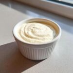 Close-up of thick, creamy garlic sauce swirled in a small white ramekin dish.
