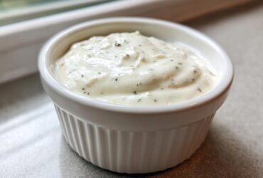 Close-up of thick, creamy garlic sauce speckled with herbs served in a small white fluted ramekin.