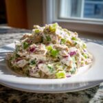 A mound of creamy healthy tuna salad mixed with diced green celery and red onion served on a white plate.