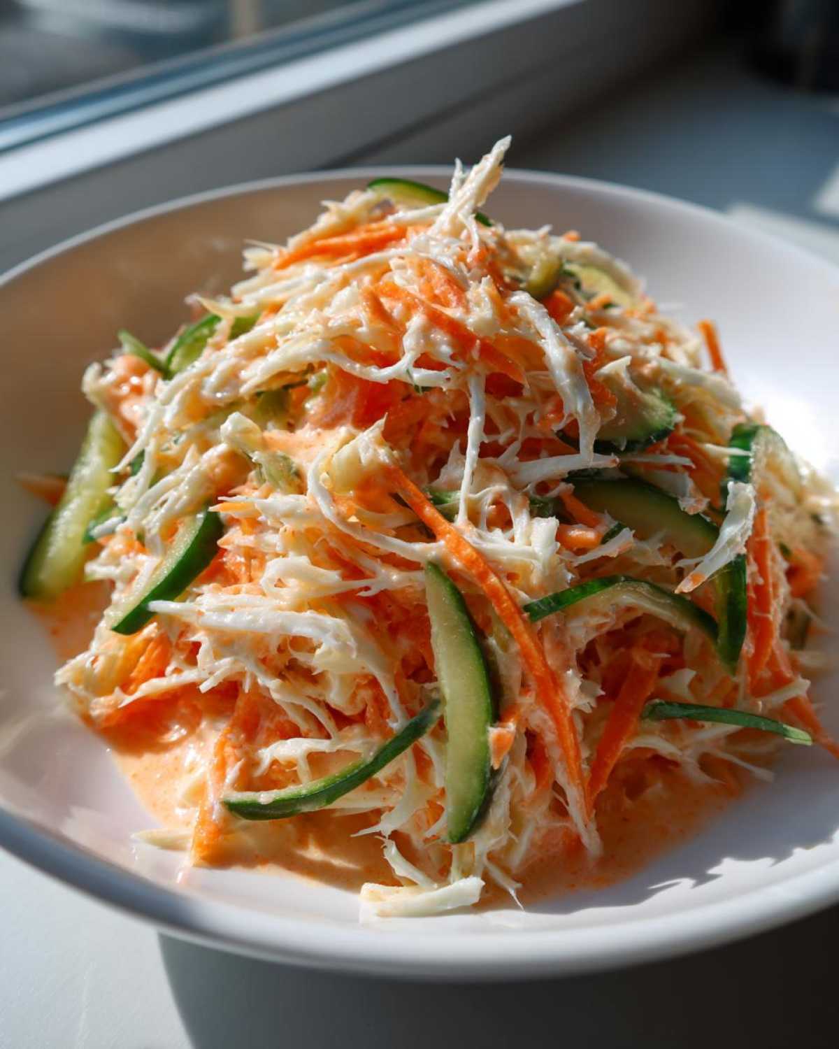 A vibrant close-up of creamy kani salad featuring shredded imitation crab, carrots, and cucumber slices.