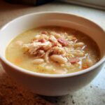 Close-up of a creamy bowl of navy bean soup topped with shredded chicken and ham pieces.