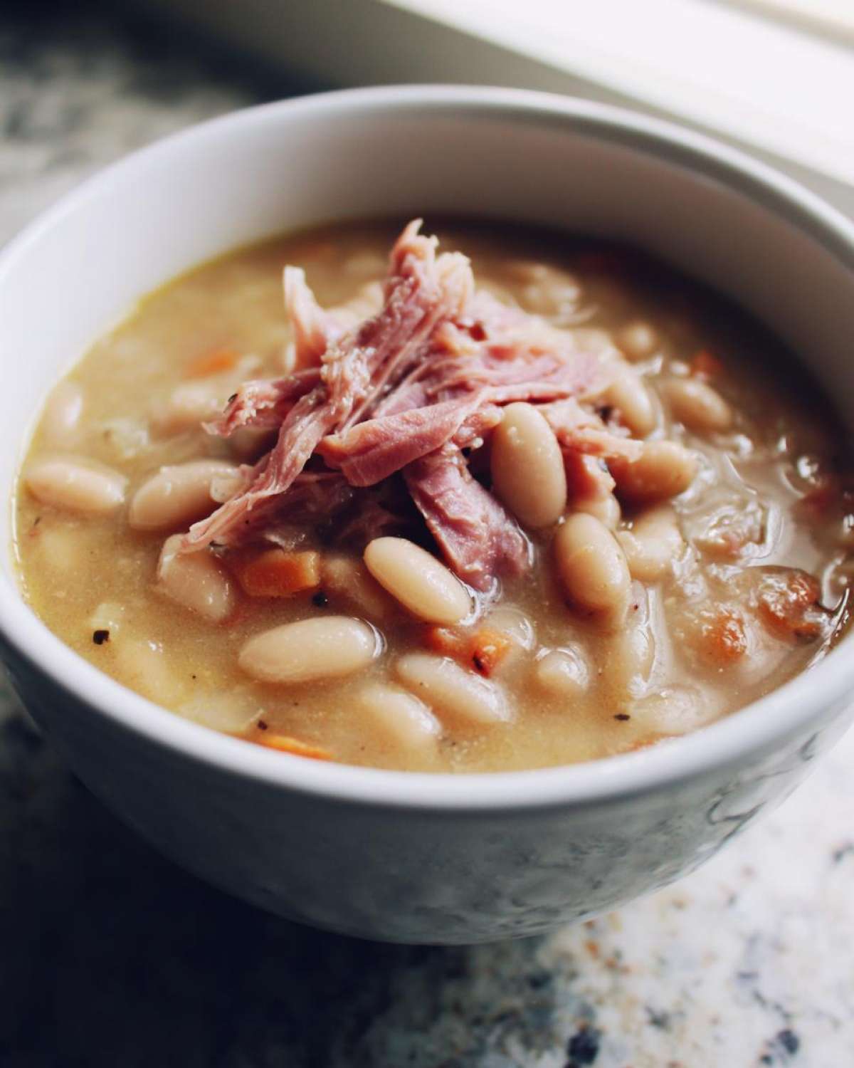 Close-up of a white bowl filled with creamy navy bean soup topped with shredded ham.