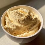 Close-up of a scoop of pale yellow, creamy protein ice cream served in a white bowl.