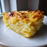 A thick, golden-brown slice of creamy scalloped potatoes with a cheesy crust on a white plate.