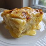 A thick, creamy slice of golden brown scalloped potatoes oozing sauce onto a white plate.