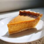 A close-up, sunlit slice of creamy sweet potato pie on a white plate.