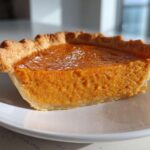A close-up of one creamy slice of sweet potato pie on a white plate.