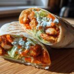 Close-up of a crispy buffalo chicken wrap cut in half, showing spicy chicken, lettuce, carrots, and blue cheese dressing.
