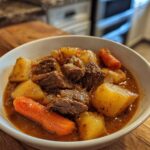 A close-up of a white bowl filled with tender chunks of beef, potatoes, and carrots in rich gravy from the crockpot beef stew.
