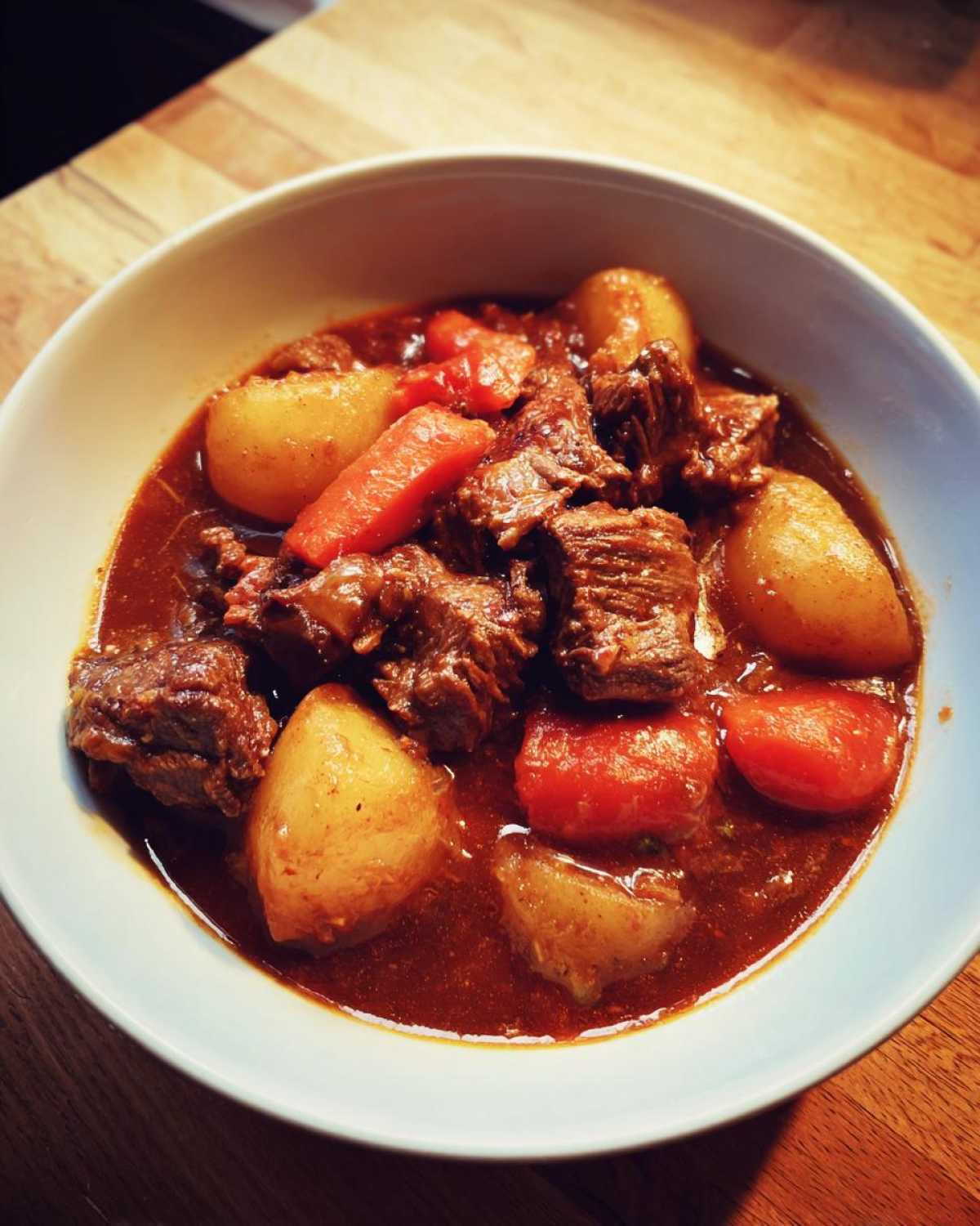 A close-up of a bowl filled with rich, dark crockpot beef stew featuring tender beef chunks, potatoes, and carrots.