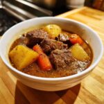 Close-up of a white bowl filled with rich crockpot beef stew featuring tender beef chunks, potatoes, and carrots.