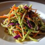 Close-up of a vibrant, crunchy cabbage salad featuring shredded green cabbage, bright orange carrots, and purple cabbage.