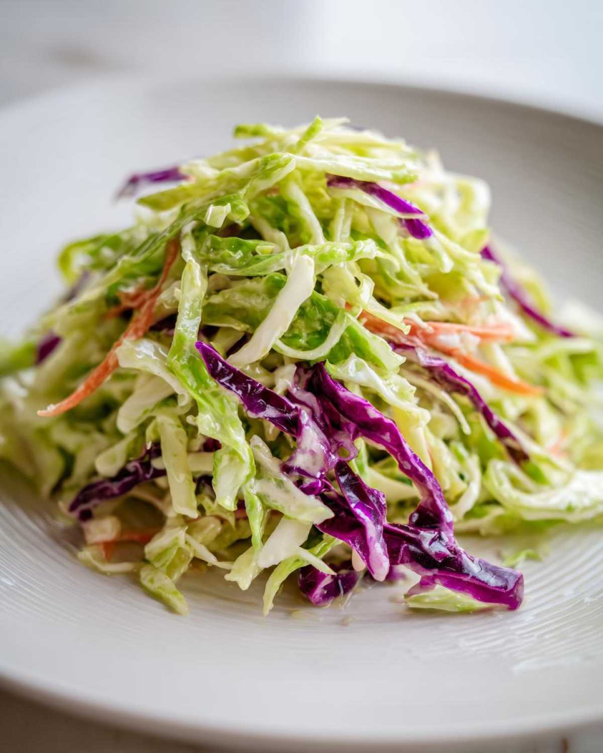 A close-up mound of creamy, crunchy cabbage salad featuring shredded green and purple cabbage and carrots.