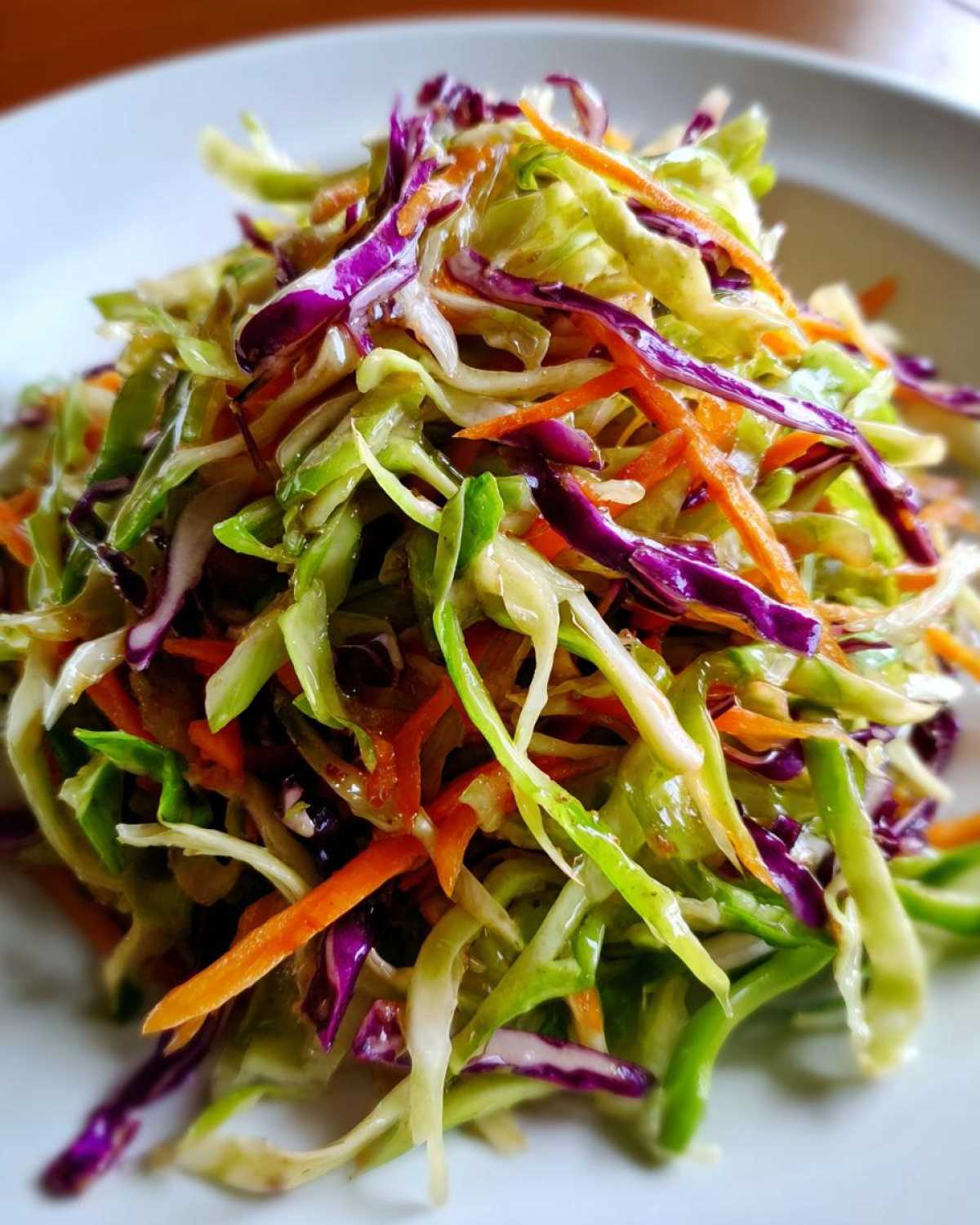 A vibrant close-up of crunchy cabbage salad featuring shredded green cabbage, purple cabbage, and bright orange carrots tossed in a light dressing.