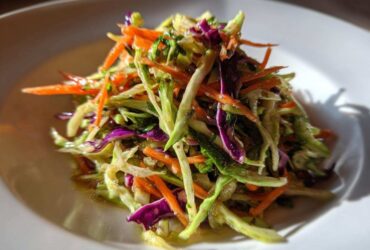 Close-up of a vibrant, crunchy cabbage salad featuring shredded green cabbage, bright orange carrots, and purple cabbage.