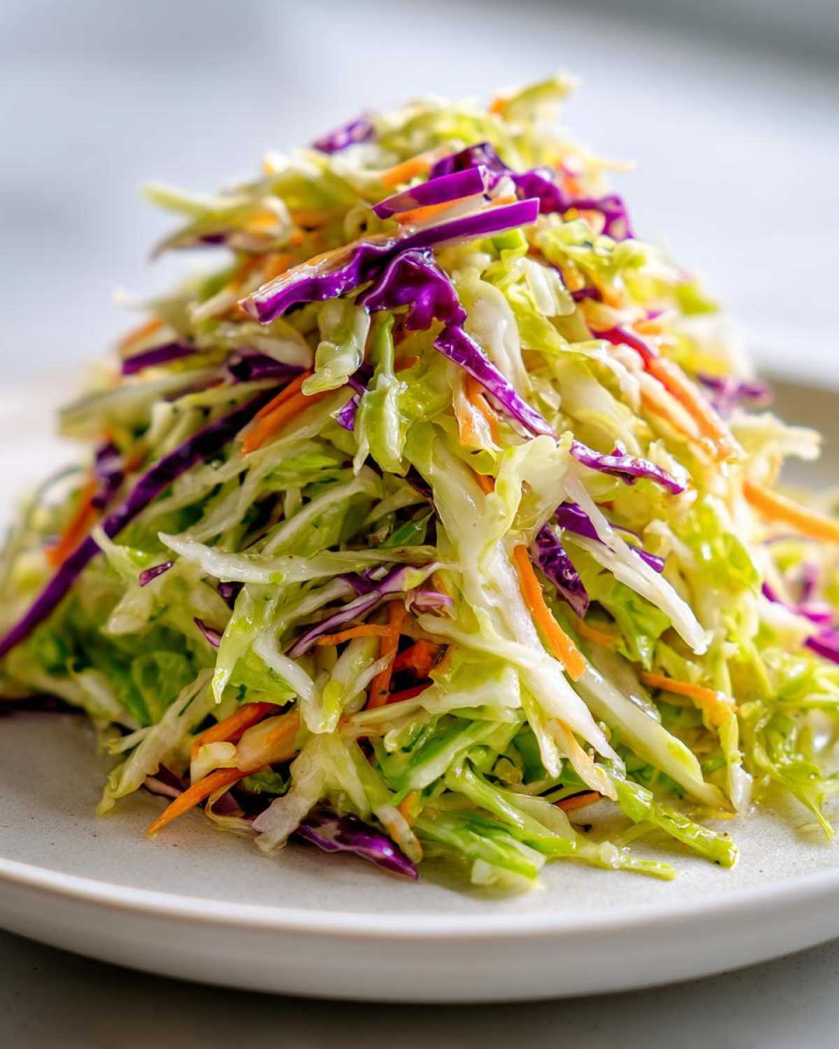 Close-up of a mound of fresh, crunchy cabbage salad featuring shredded green cabbage, purple cabbage, and carrots.