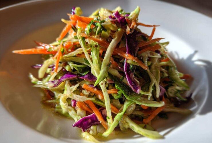 Close-up of a vibrant, crunchy cabbage salad featuring shredded green cabbage, bright orange carrots, and purple cabbage.