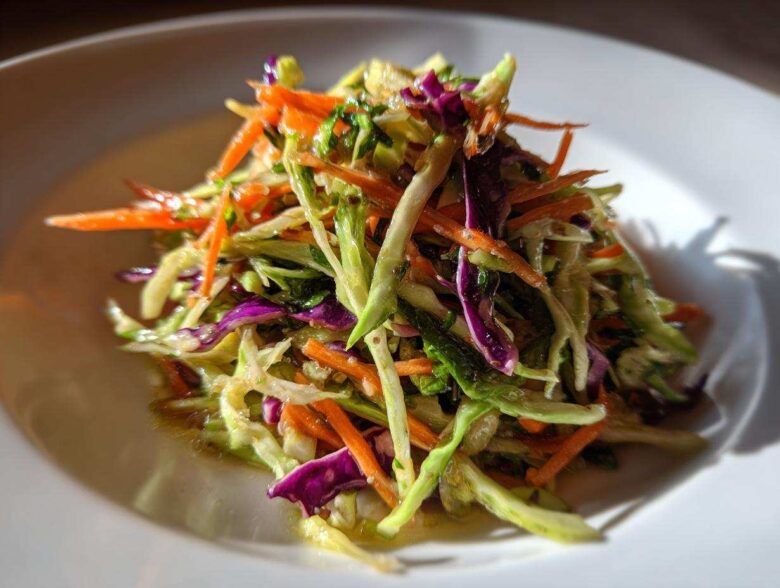 Close-up of a vibrant, crunchy cabbage salad featuring shredded green cabbage, bright orange carrots, and purple cabbage.