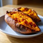 Close-up of two perfectly baked sweet potatoes, split open to show the fluffy, orange interior seasoned with pepper.