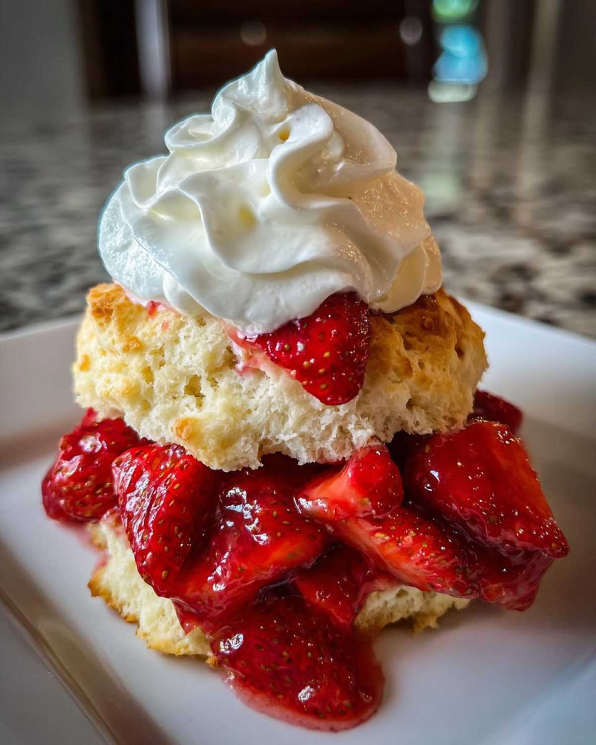 Close-up of a fluffy shortcake split and filled with macerated strawberries, topped with whipped cream.