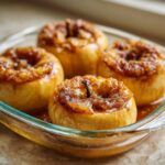 Four golden baked apples served in a glass dish, topped with a glistening brown sugar and spice mixture.