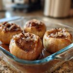 Four perfectly baked apples with a crumbly cinnamon sugar topping sitting in a glass baking dish.
