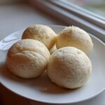Four perfectly shaped balls of smooth fufu served on a white plate near a window.