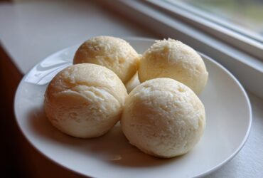 Four perfectly shaped balls of smooth fufu served on a white plate near a window.