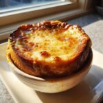 Close-up of a bowl of french onion soup recipe topped with a thick layer of golden, bubbly, broiled cheese.