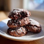 A stack of four rich, dark chocolate hot chocolate cookies dusted generously with powdered sugar.
