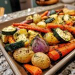 Close-up of vibrant Garlic Herb Roasted Veggies including potatoes, carrots, zucchini, and red onion on a baking sheet.