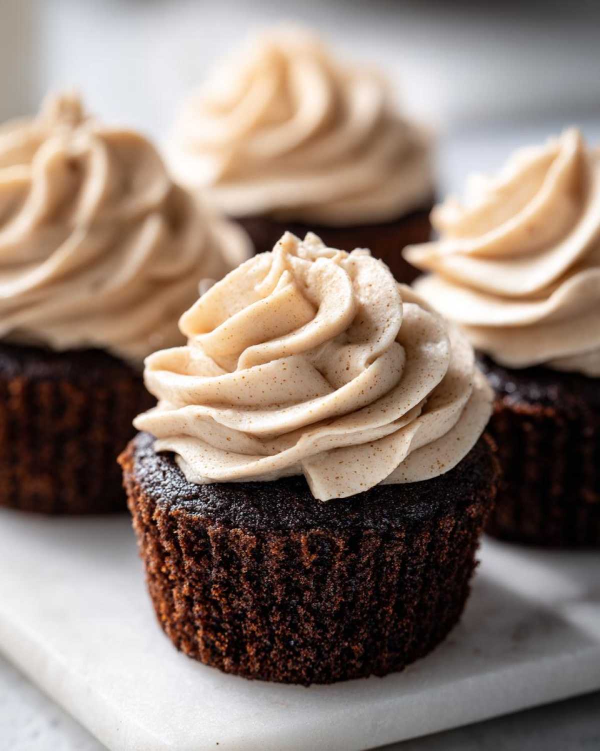 A close-up of a rich, dark gingerbread cupcake topped with swirled, spiced cream cheese frosting.