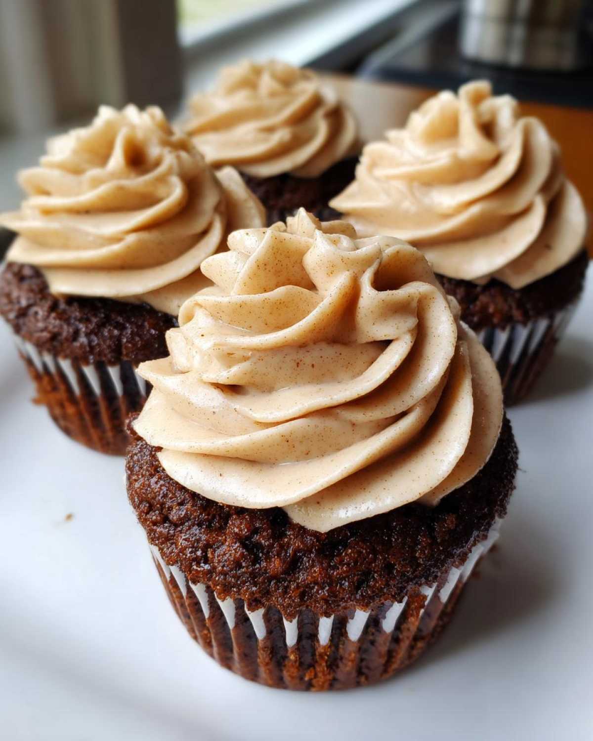 A close-up of four rich, dark gingerbread cupcakes topped with swirls of spiced cream cheese frosting.