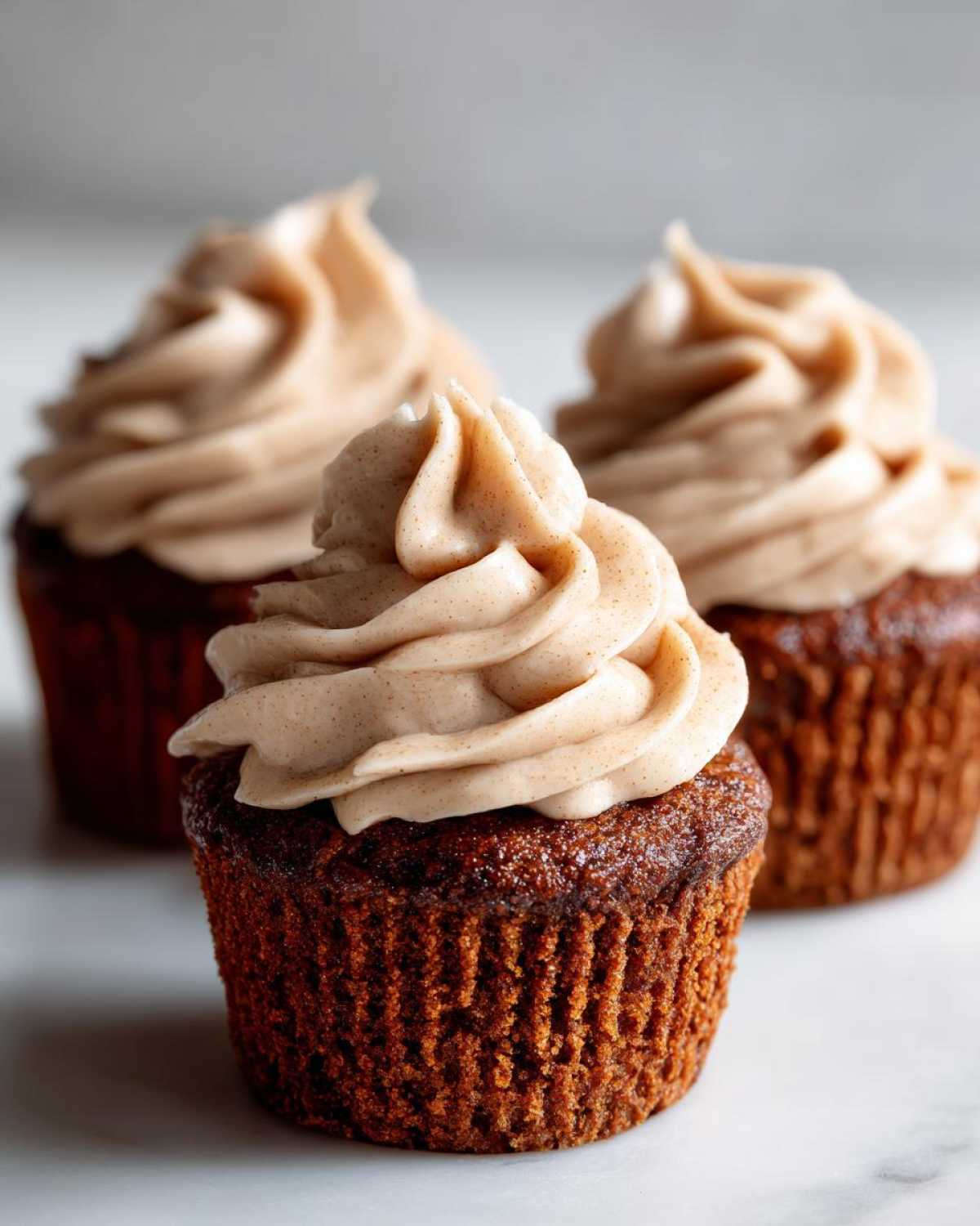 Three rich, dark gingerbread cupcakes topped with swirls of spiced cream cheese frosting, photographed closely.