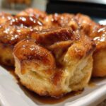 Close-up of freshly baked, golden-brown rolls covered in a shiny caramel glaze, resembling an apple dumpling dessert.