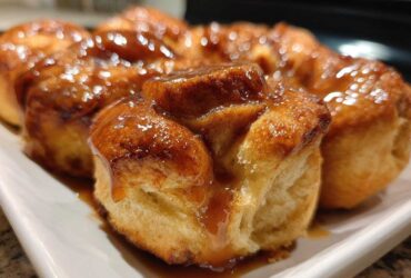 Close-up of freshly baked, golden-brown rolls covered in a shiny caramel glaze, resembling an apple dumpling dessert.