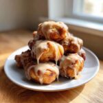 A stack of golden brown baked apple fritters generously drizzled with a thick, creamy glaze.