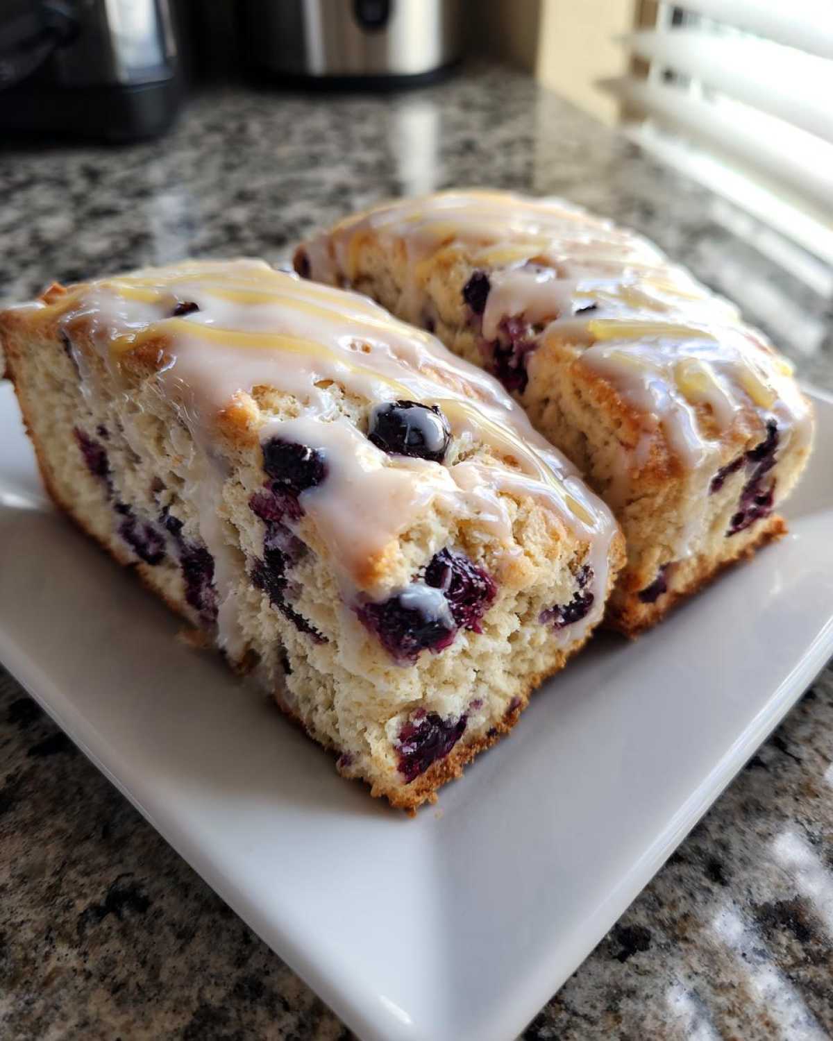 Two thick, bakery-style blueberry scones topped with a sweet white glaze, resting on a white plate.