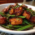 Close-up of glazed, saucy chicken pieces mixed with bright green beans, a featured dish of chicken and green beans.
