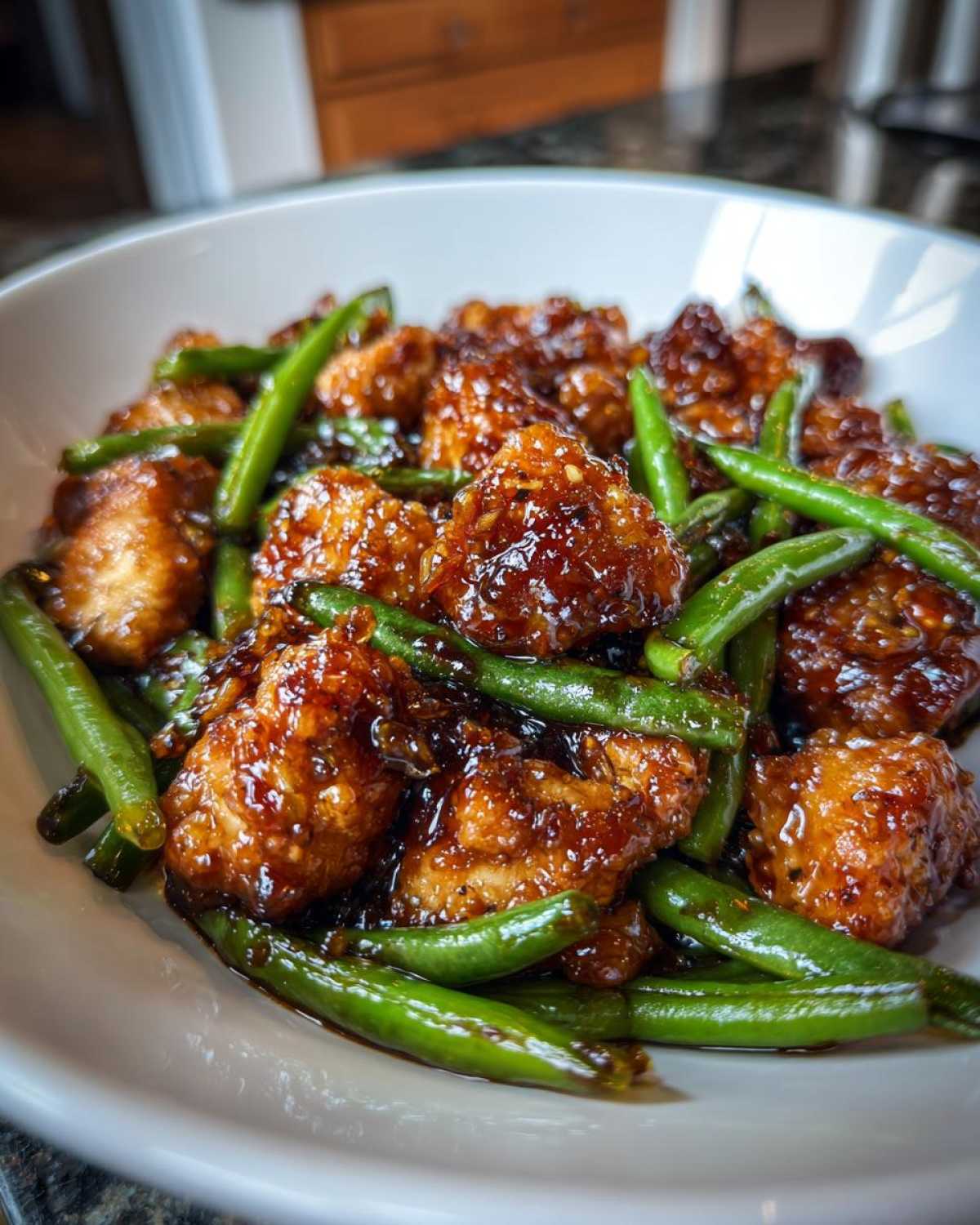 Close-up of glazed, saucy chicken pieces mixed with bright green beans, a perfect chicken and green beans dinner.