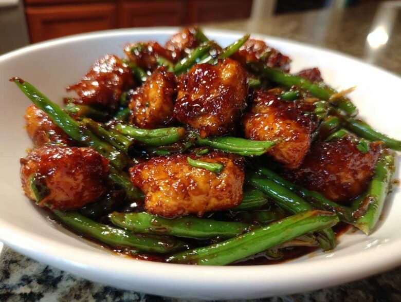 Close-up of glazed, saucy chicken pieces mixed with bright green beans, a featured dish of chicken and green beans.