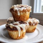 A stack of three delicious cinnamon roll muffins topped with thick white icing dripping down the sides.