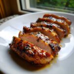 Close-up of perfectly cooked and sliced pork tenderloin recipe with a shiny, savory glaze and herbs.