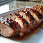 Close-up of perfectly cooked, sliced pork tenderloin recipe with a shiny, dark glaze resting in its juices.