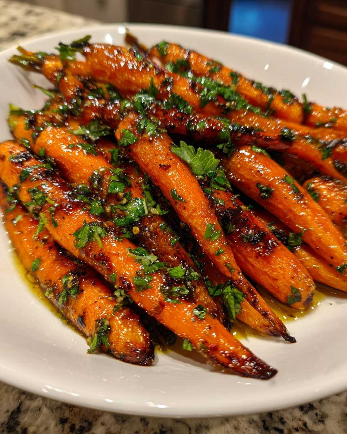 A close-up of glossy, glazed roasted carrots topped with chopped fresh parsley in a white bowl.
